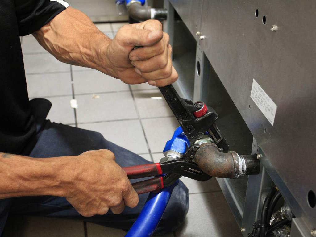 A man using a wrench to repair a pipe, focused on fixing the plumbing issue with determination.