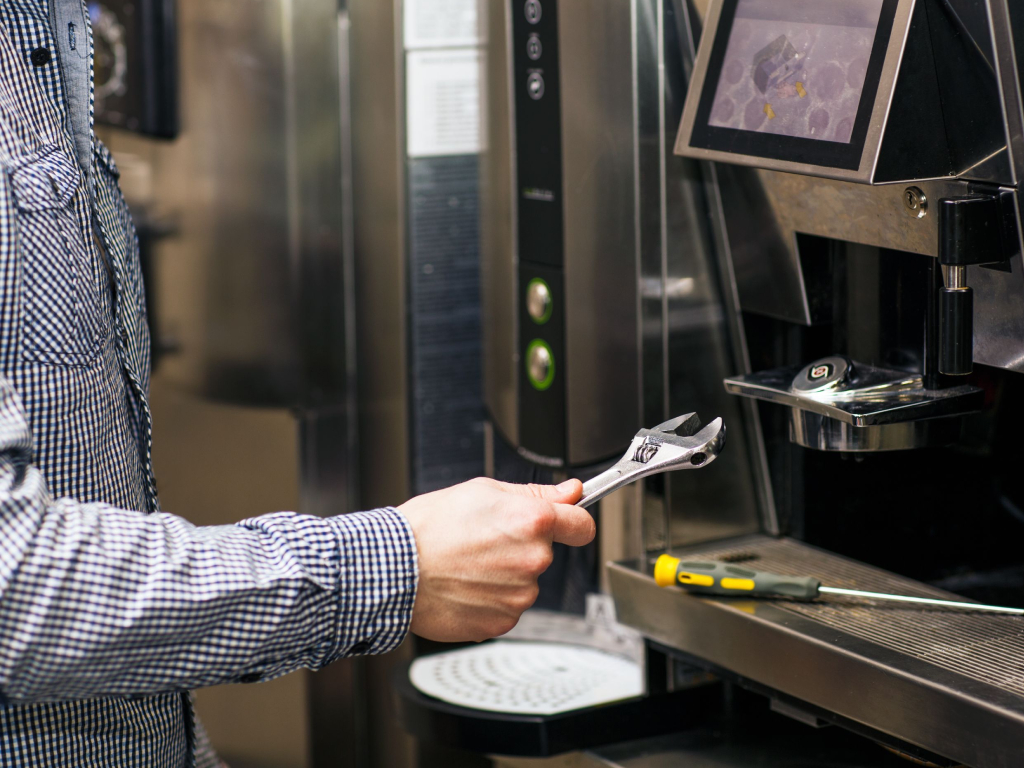 A man repairs a coffee machine with a wrench, focused on fixing the appliance in a cozy kitchen setting.