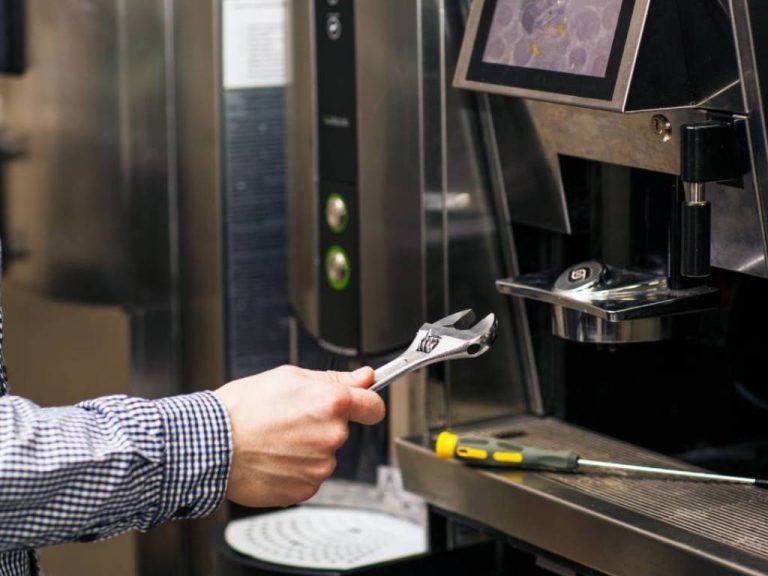 A man repairs a coffee machine with a wrench, focused on fixing the appliance in a cozy kitchen setting.